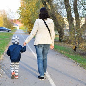 A mother and toddler walk down a path in the suburbs.