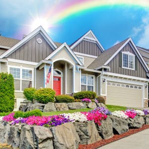 A suburban home with a landscaped yard and a rainbow above it.