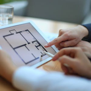 Hands holding a tablet with a floor plan on it