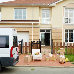 A house with a moving van parked outside and boxes on the sidewalk.