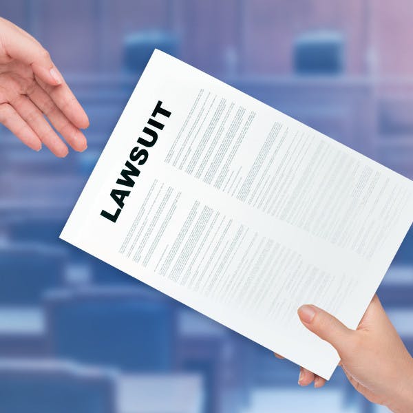 Image of hands handing a document that reads lawsuit to another person.