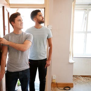 A male millennial couple opens the door of their new home.