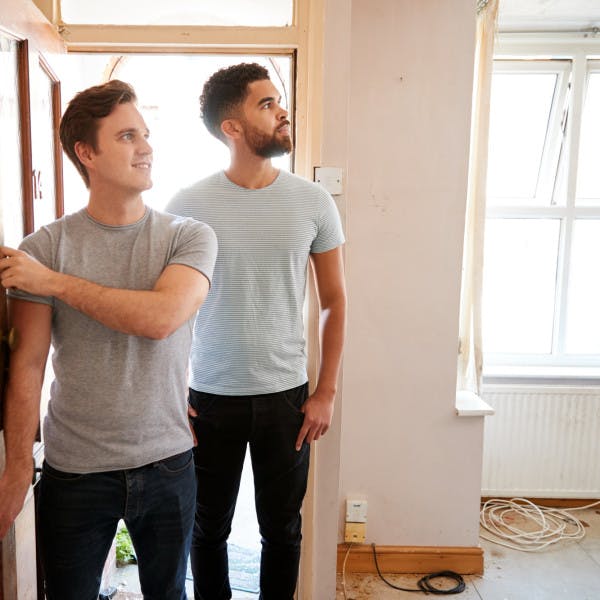 A male millennial couple opens the door of their new home.