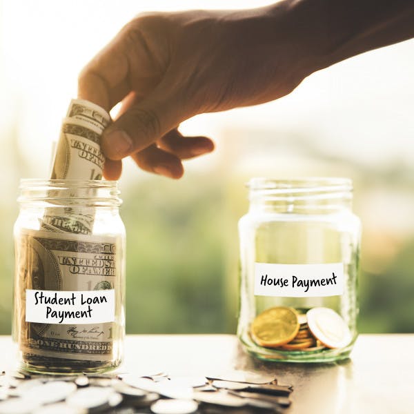 A person puts money in a jar labeled "student loan payment" instead of a jar labeled "house payment."