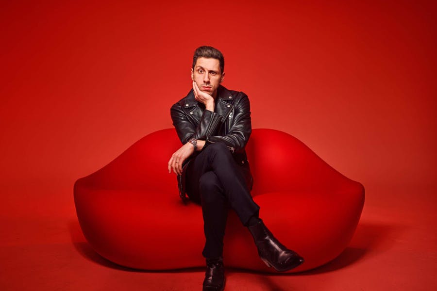 Matt Lionetti, a real estate agent with The Agency Toronto West, poses on a red lip-shaped couch.
