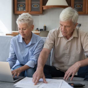 An older couple looks at financial papers and a laptop. 