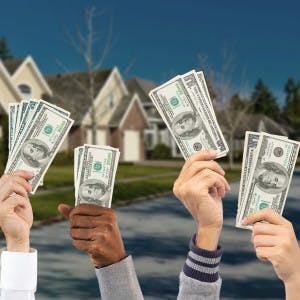 Outreached hands holding dollar bills with houses in the background