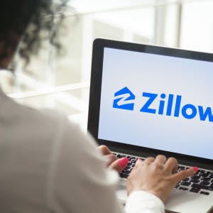 Woman viewing laptop screen that shows Zillow logo