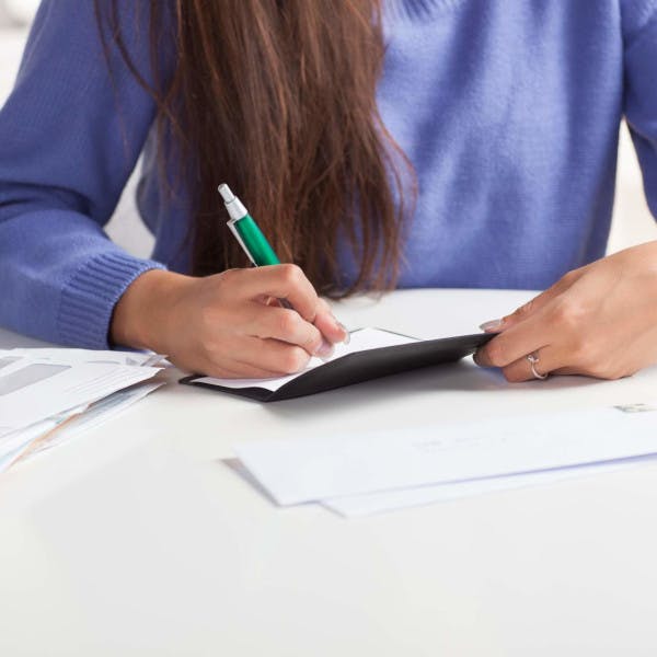 A woman sits at a table writing a check.