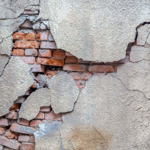 A cracked cement facing reveals the bricks underneath in an exterior wall.