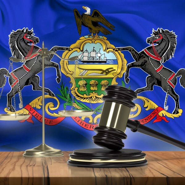 The state flag of Pennsylvania behind a gavel and scales of justice.