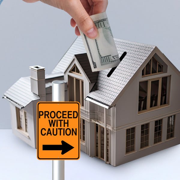 Putting money into a house with a 'proceed with caution' sign in front.