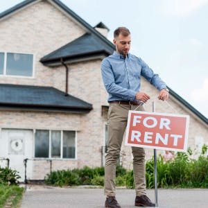 A real estate agent hangs a "for rent" sign in front of a home.