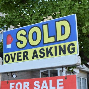 A for-sale sign with a "sold over asking" addendum in front of a house.