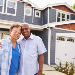 Diverse older couple standing in front of house