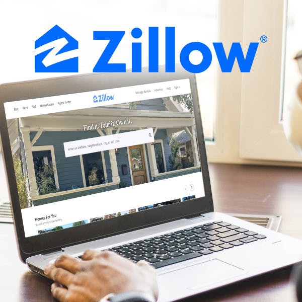 A man looking at the Zillow home page on his laptop.