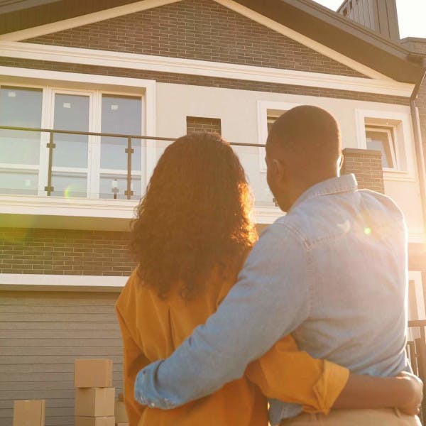 A Black couple stands in front of a home at sunset.