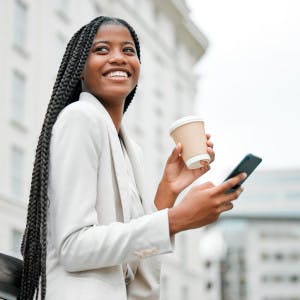 A happy young Black real estate agent holds her phone and a cup of coffee while on the go.