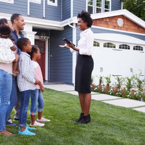 A real estate agent talking with a family in front of a home for sale.